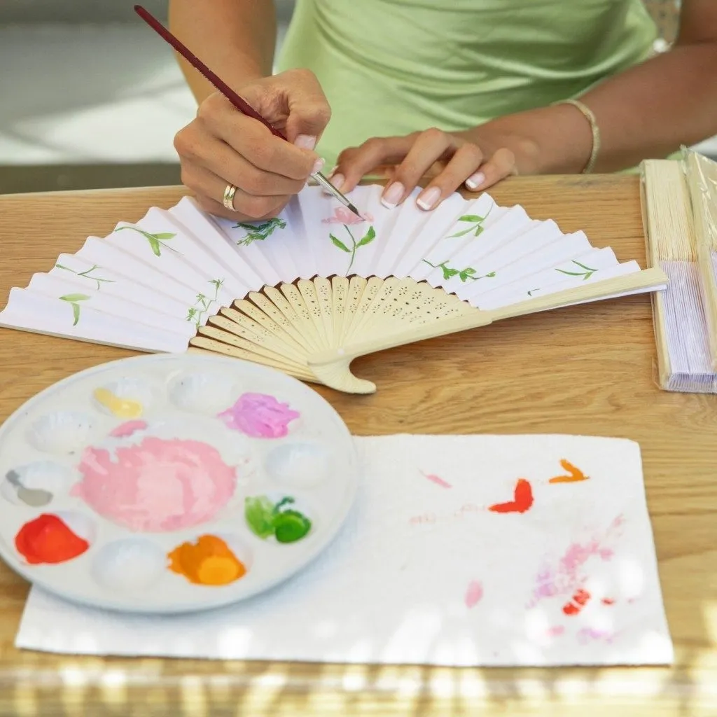 Éventail en papier peint à la main avec des fleurs, palette de peinture posée à côté